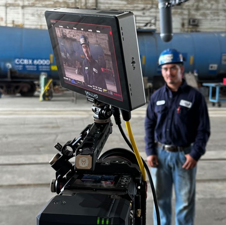 Man in a hard hat on a camera monitor with a railroad car in the background for Workplace Safety Training Videos in Memorial