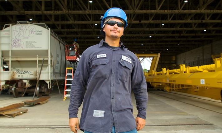 Male worker in a blue hard hat and safety glasses standing in a train yard for Workplace Safety Training Videos in Memorial