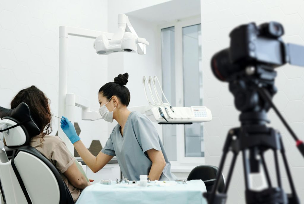Female dentist treating a patient in a clinic while a camera records the procedure for Dental Practice Marketing Videos Houston.