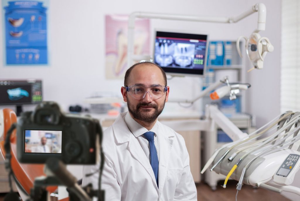 A male dentist in a lab coat and goggles in a clinic, ideal for Dental Practice Marketing Videos Houston.