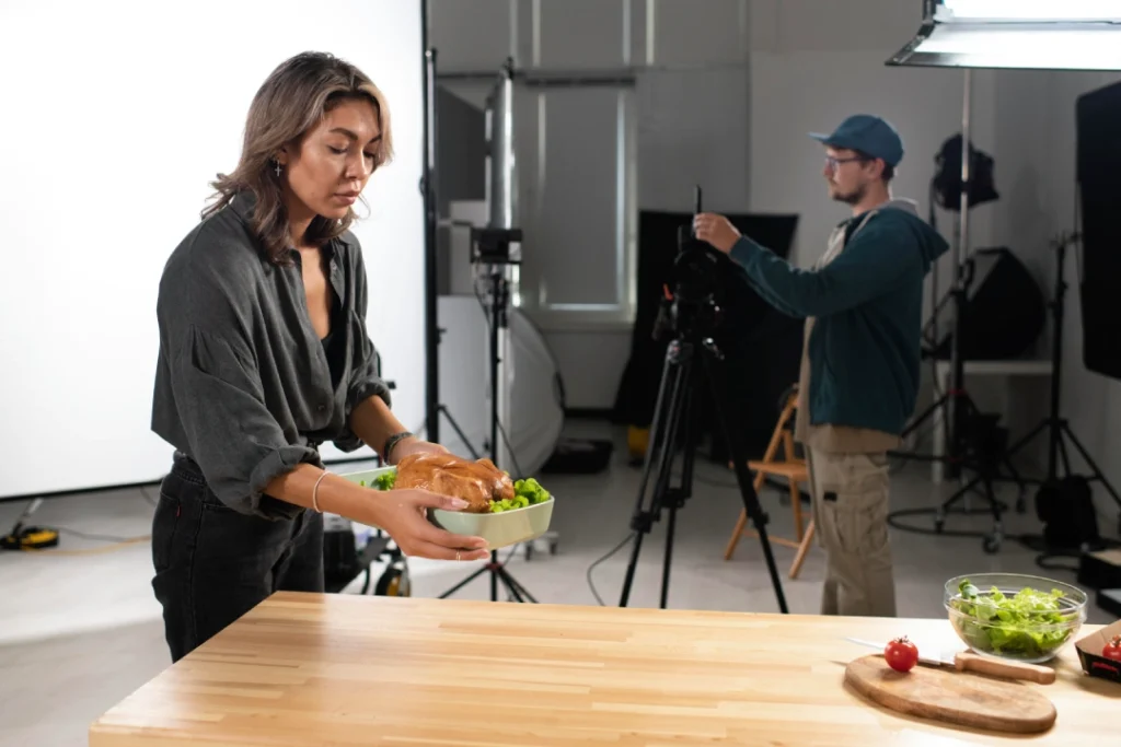 Woman presenting a chicken dish on set while filmed by crew for Commercial Video Production Houston, showcasing expert food videography techniques.