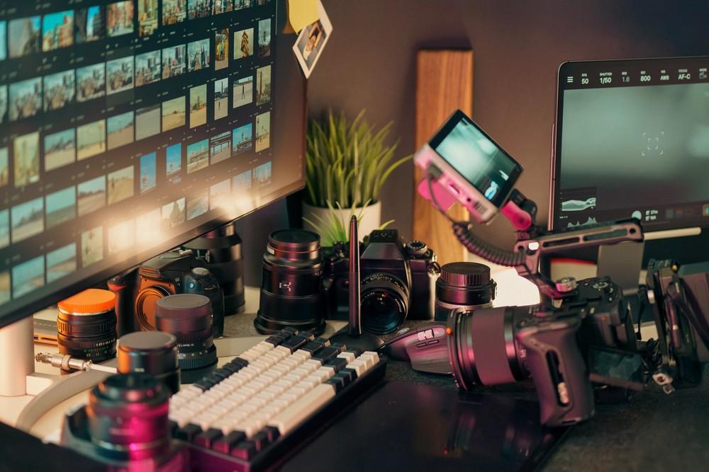High-end editing workspace of a professional videography company Houston with dual monitors, multiple cameras, and a full lens kit.