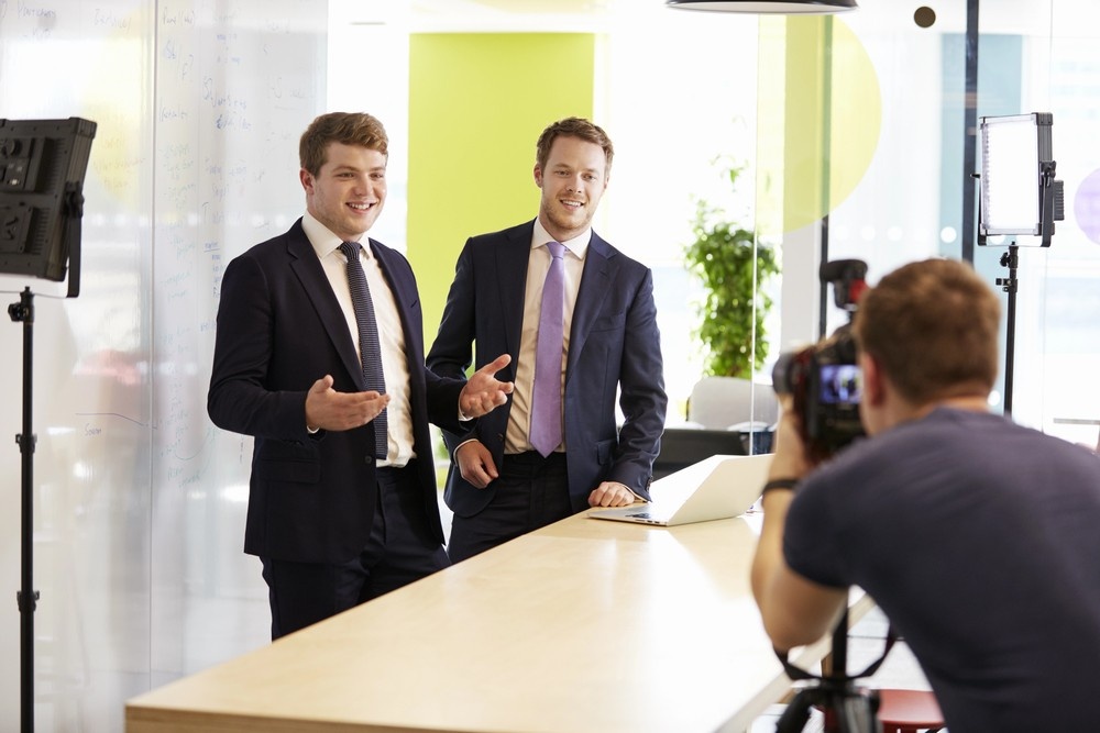 Two smiling young Houston executives presenting, with a professional industrial video production Houston crew filming.